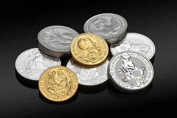 Royal Mint Queen's Beasts gold and silver bullion coins arranged on a dark reflective surface.